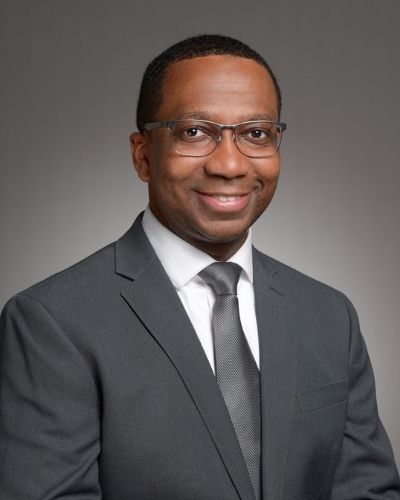 A headshot of Dr. Walter Conwell. A Black man in a gray suit and tie in front of a gray background.